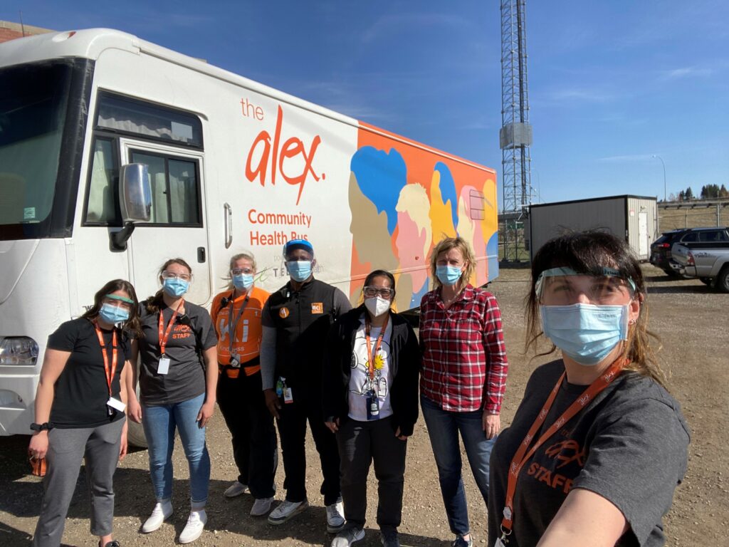 Photo of a group of Alex staff in front of the Community Health Bus, where they administer vaccines